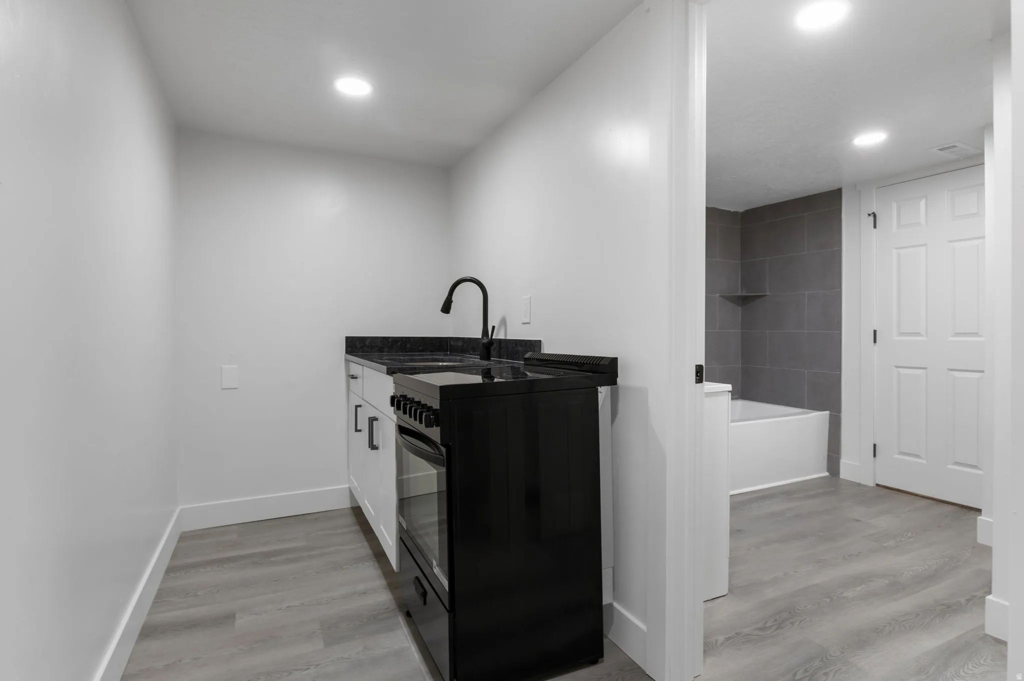 Compact kitchen area featuring white cabinetry, a black range, and a black faucet with a coordinating dark countertop