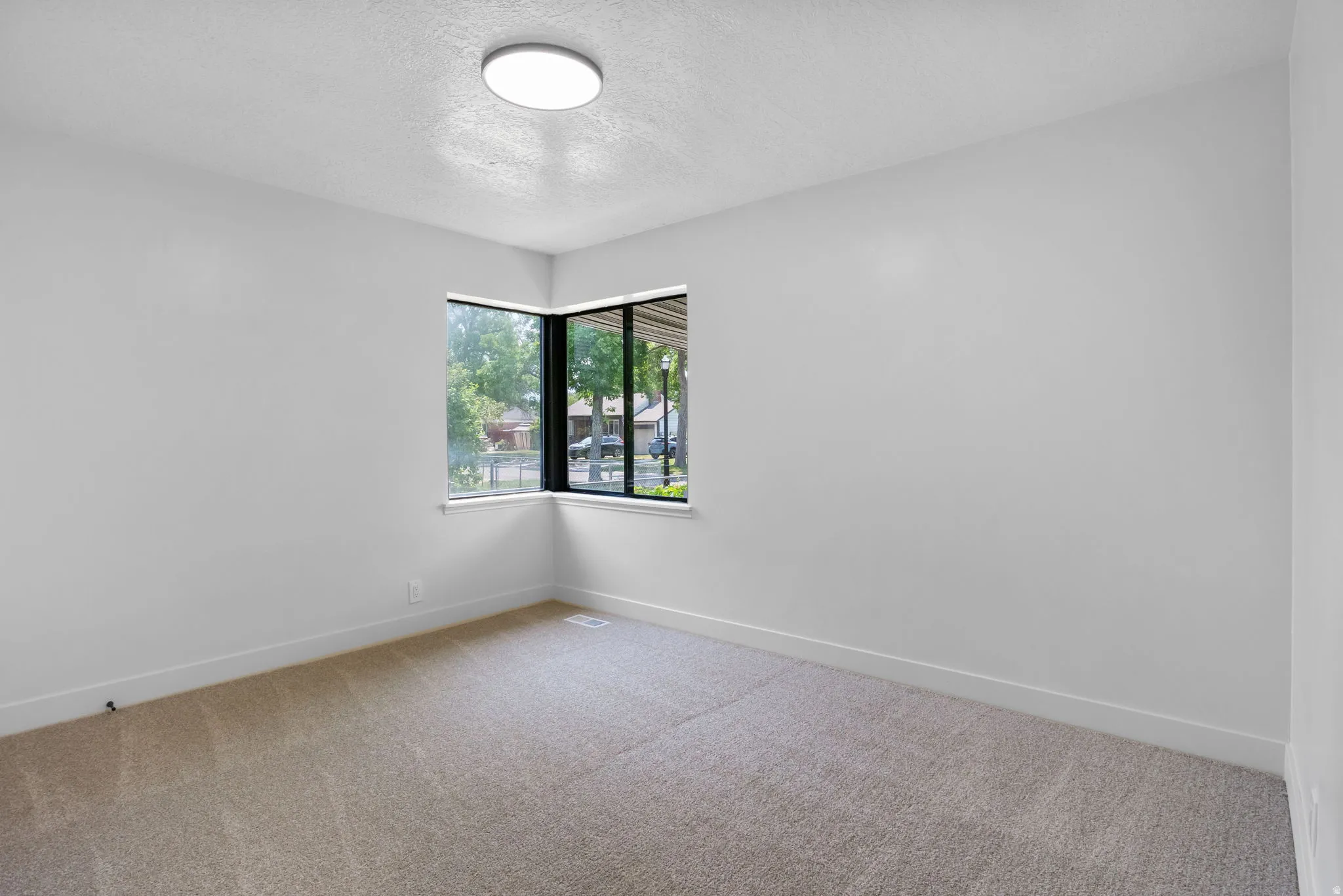 Neutral wall color throughout this space, featuring a corner window with black frames, recessed heating vent, and a flush mount ceiling light