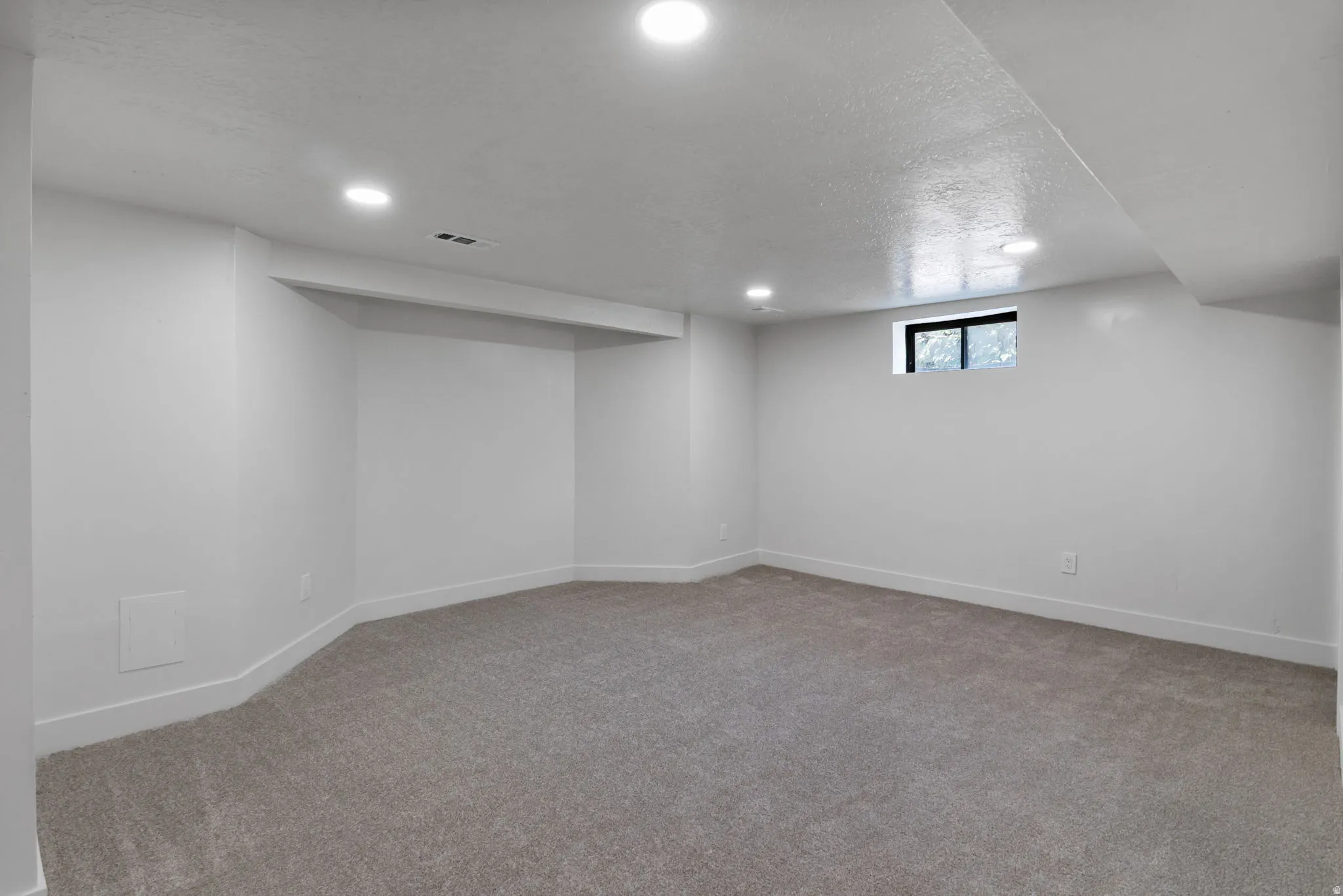 Spacious room featuring new gray carpeting, white painted walls, recessed lighting, and a single egress window