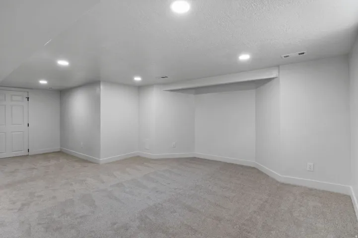 Spacious room featuring light gray carpeting, crisp white walls, recessed ceiling lighting, and a built-in alcove