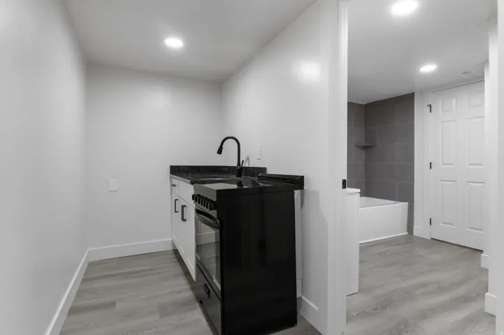 Compact kitchen area featuring white cabinetry, a black range, and a black faucet with a coordinating dark countertop
