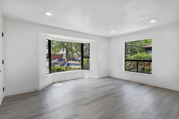 Spacious room featuring a prominent bay window with black frames, wood-finish flooring, recessed lighting, and crisp white walls