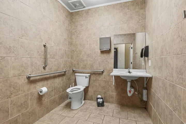 Tile-finished restroom featuring a wall-mounted sink, a toilet, and stainless steel grab bars