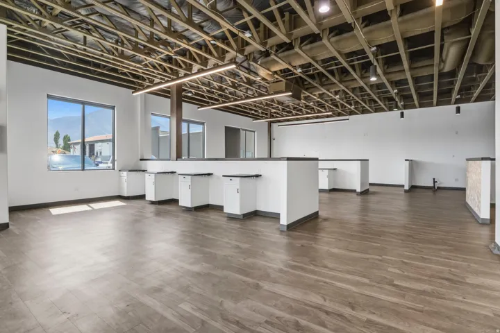 Spacious commercial interior featuring exposed ceiling trusses and ductwork, wood-finish flooring, and multiple large windows