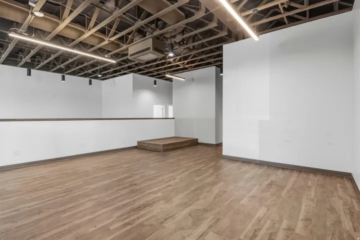 Open-concept commercial space featuring wood-finish flooring, exposed ceiling trusses, and recessed lighting