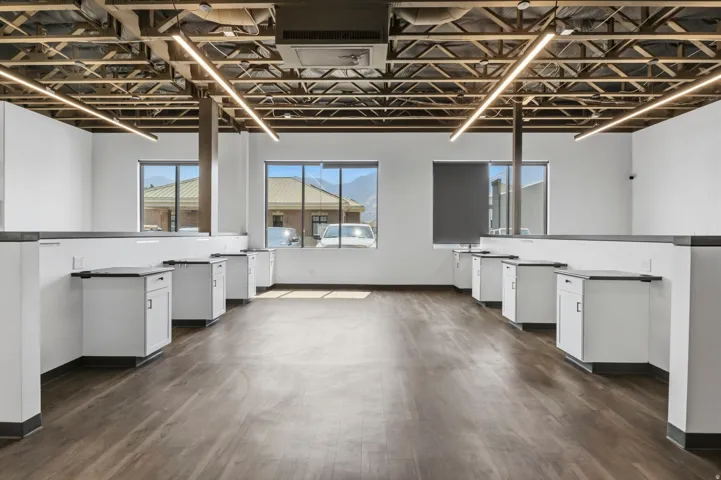 Open-concept space featuring exposed ceiling joists, linear pendant lighting, wood-finish flooring, multiple windows, and built-in cabinetry with dark countertops