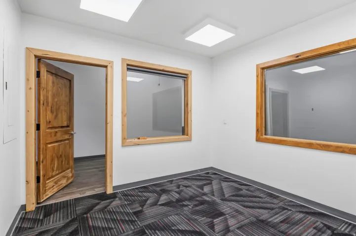 Room featuring wood-finish door and trim, patterned carpet flooring with a dark border, and two rectangular interior windows