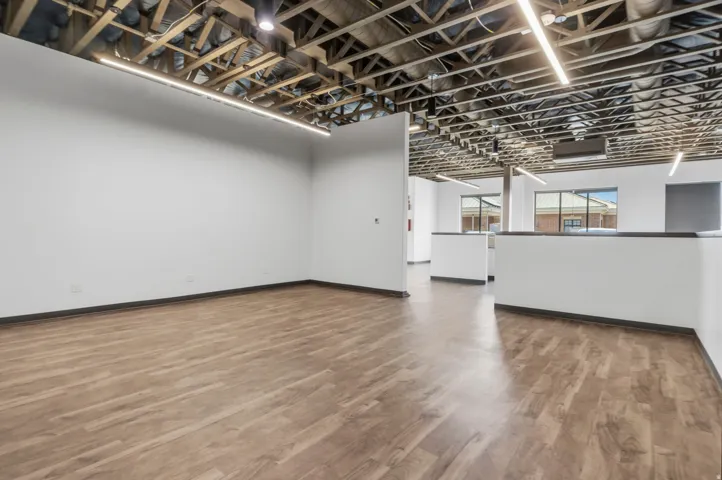 Expansive open-concept room featuring wood-finish flooring, white walls, and an exposed ceiling with linear light fixtures