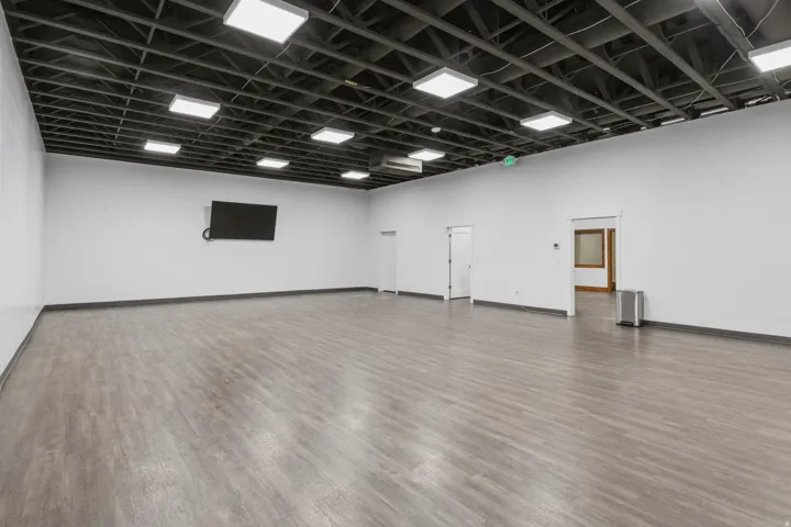 Spacious room featuring wood-finish flooring, white walls, and an exposed ceiling with recessed lighting