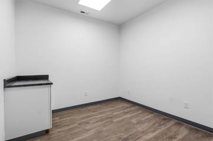 Room featuring wood-finish flooring, white walls, and a built-in corner cabinet with a dark countertop