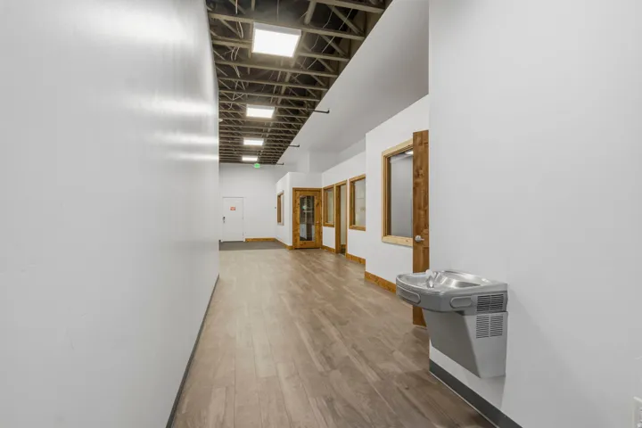 Hallway featuring wood-finish flooring, exposed ceiling beams, recessed lighting, and office entrances with wood-frame windows