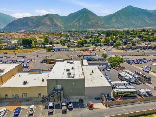 Commercial property featuring multiple buildings with flat roofs, extensive paved parking areas, and a concrete perimeter fence