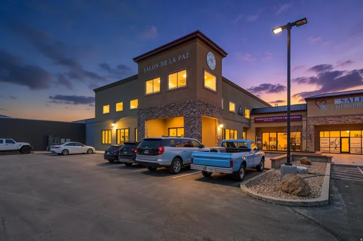 Commercial building featuring a stone facade accent, multiple large windows, exterior lighting, an integrated clock tower, and a spacious asphalt parking lot