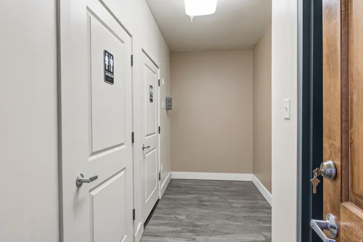 Corridor featuring wood-finish flooring, light tan walls, white baseboards, and overhead lighting