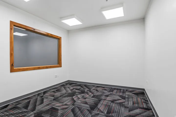 Room featuring a large interior window with a natural wood frame, white walls, and geometric pattern carpet flooring