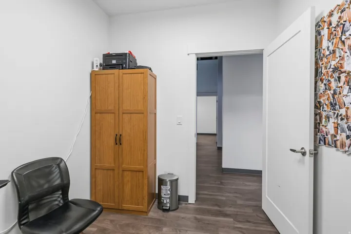 Interior space featuring wood-finish flooring, white walls, and a solid white door with satin nickel hardware