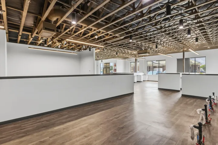Open-concept interior featuring wood-finish flooring, exposed ceiling joists, recessed and linear lighting fixtures, white partition walls, and multiple window openings