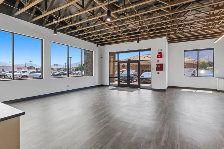 Spacious interior featuring exposed wood-truss ceiling, large storefront windows, and wood-finish flooring