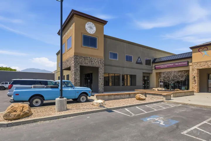 Commercial building featuring a stone and stucco exterior, prominent storefront windows, a paved parking area, and decorative stone planters