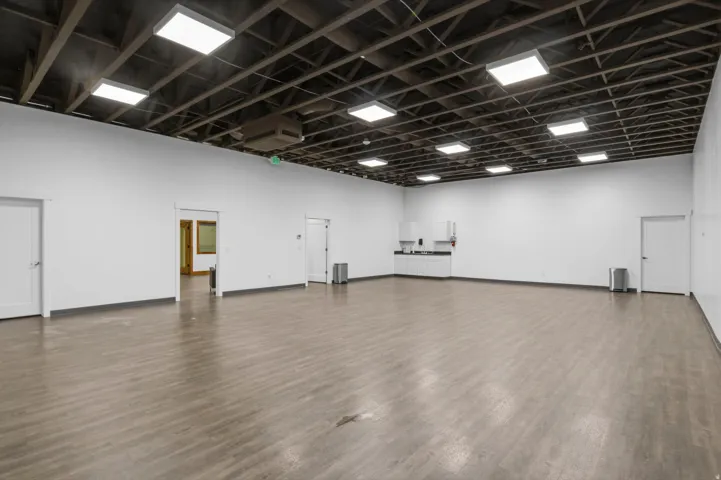 Spacious open-concept interior featuring light wood-finish flooring and exposed ceiling trusses