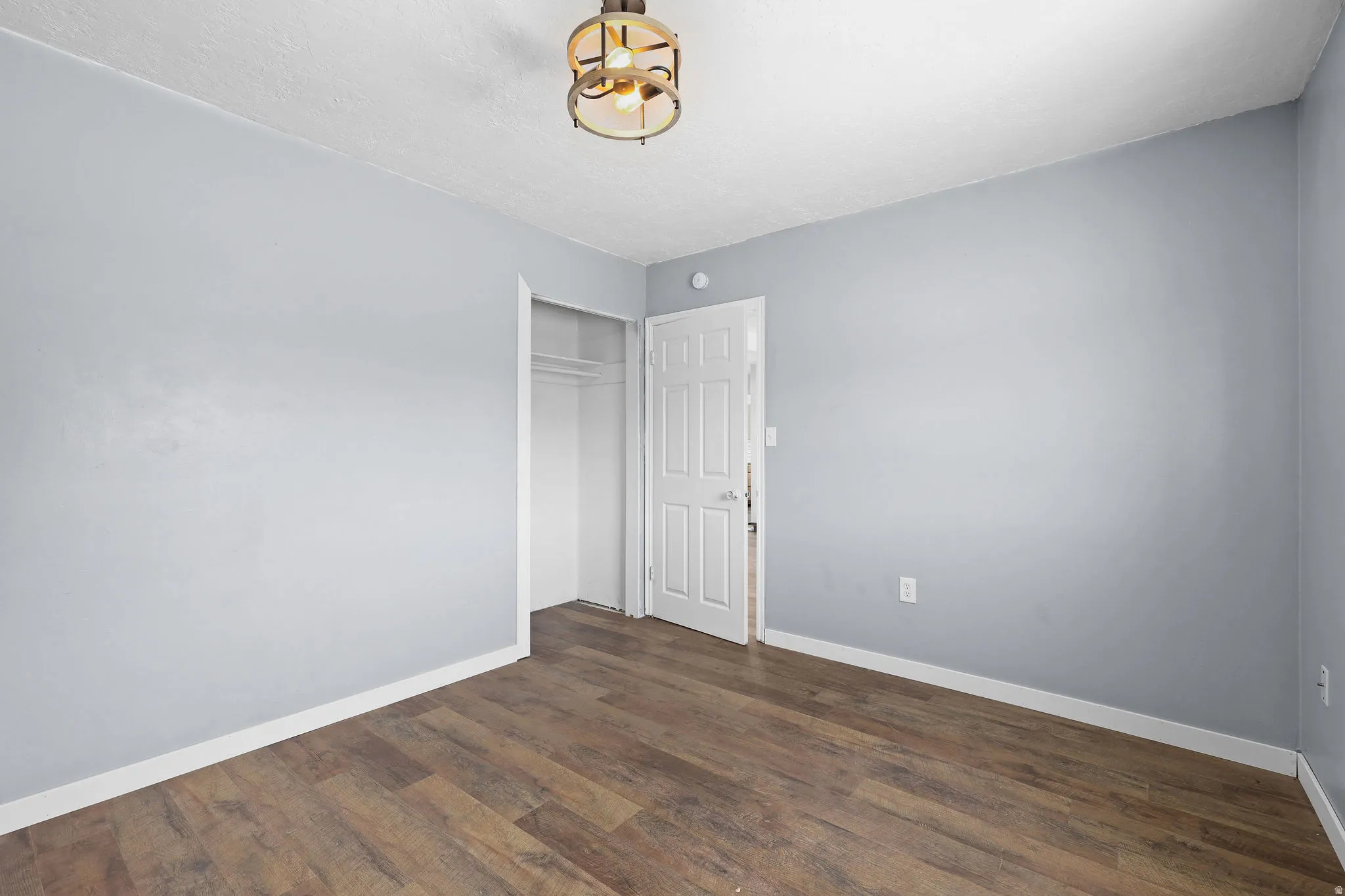 Room featuring wood-finish flooring, light blue wall paint, white trim, and a ceiling-mounted light fixture