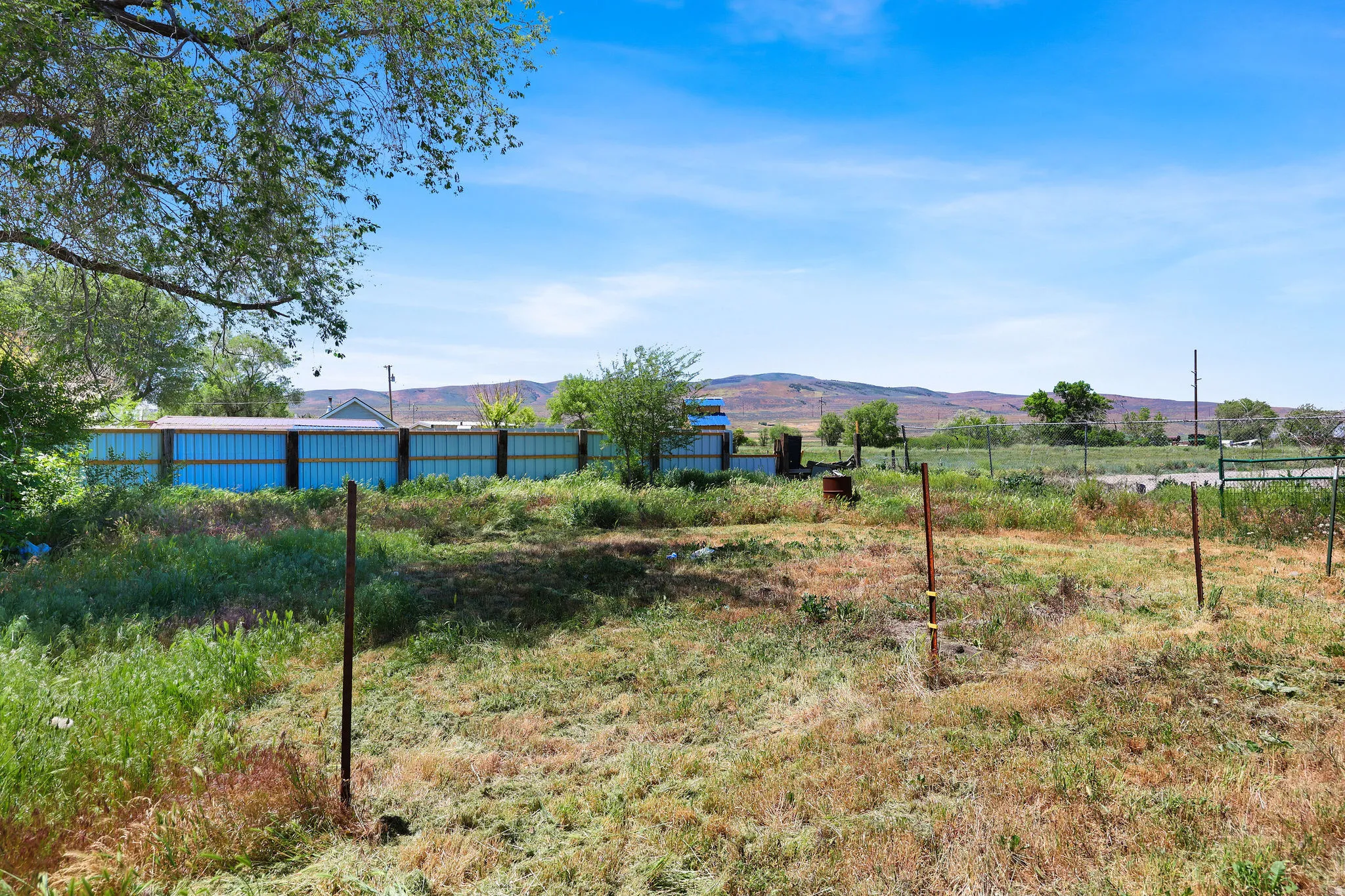 Expansive open lot featuring a clear blue sky, distant hills, and established perimeter fencing