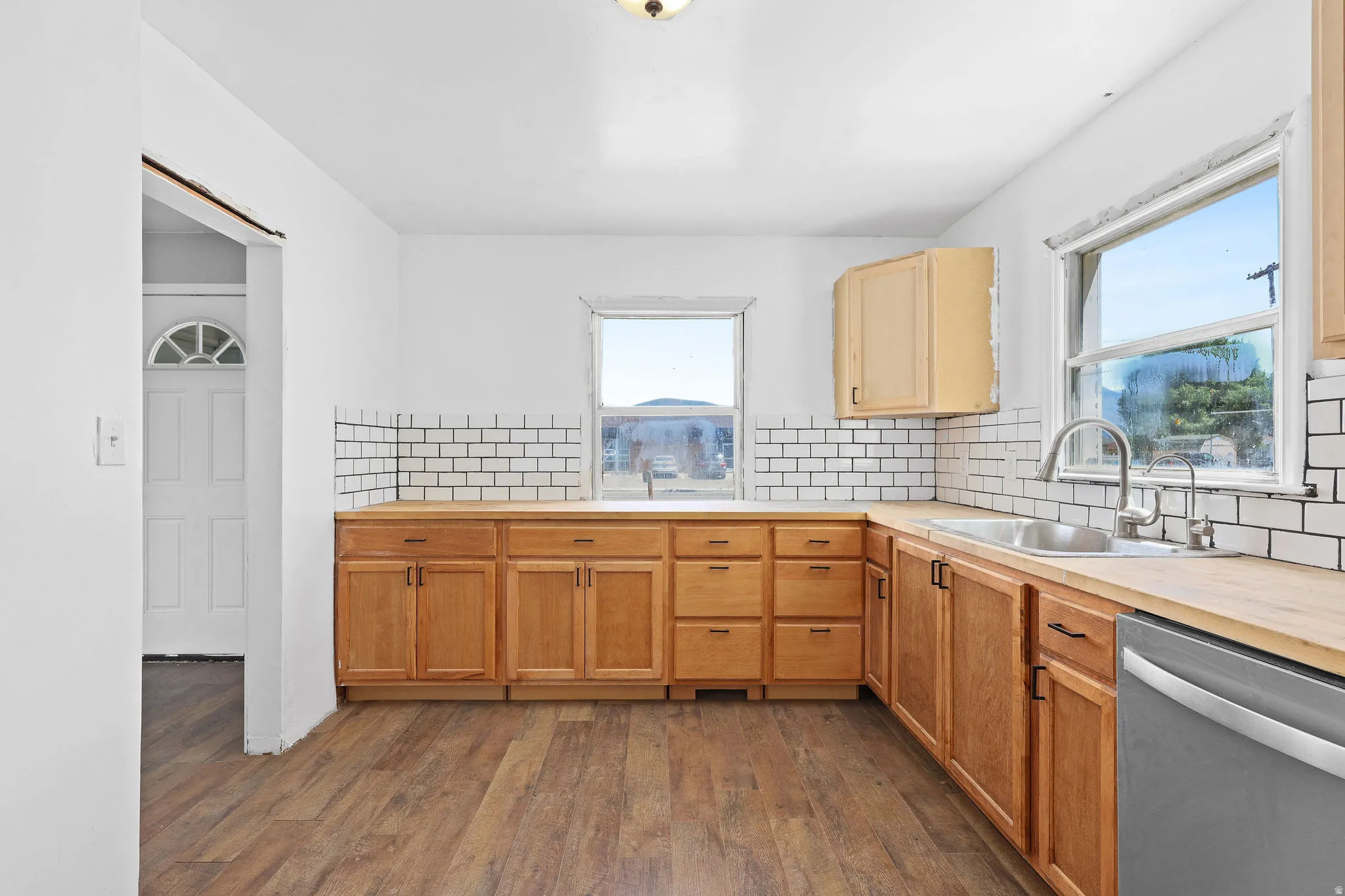 Kitchen featuring wood-finish flooring, wood cabinetry, white subway tile backsplash, stainless steel sink with gooseneck faucet, and a stainless steel dishwasher
