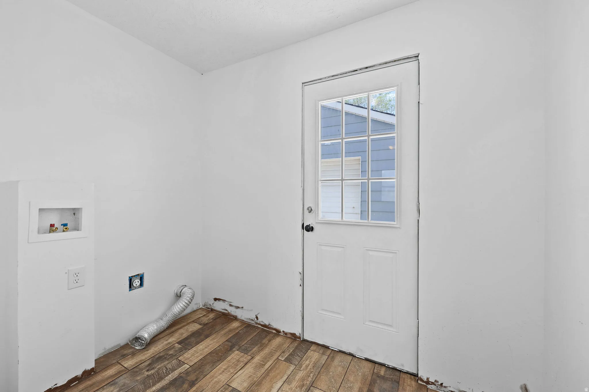 Utility space featuring wood-finish flooring and a white paneled door with grid-patterned glass