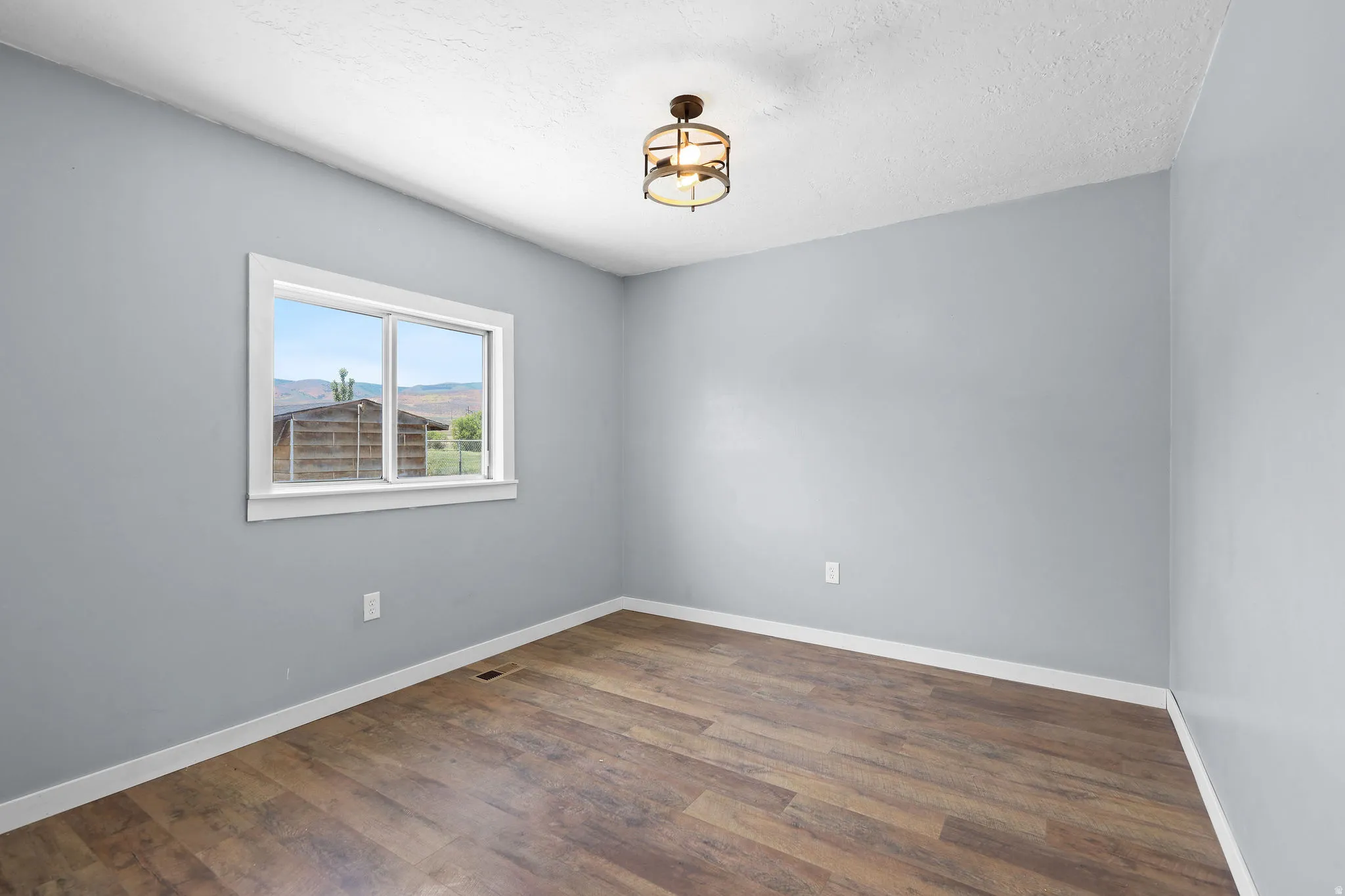 Spacious room featuring wood-finish flooring, light gray walls, white trim, and a contemporary ceiling light fixture
