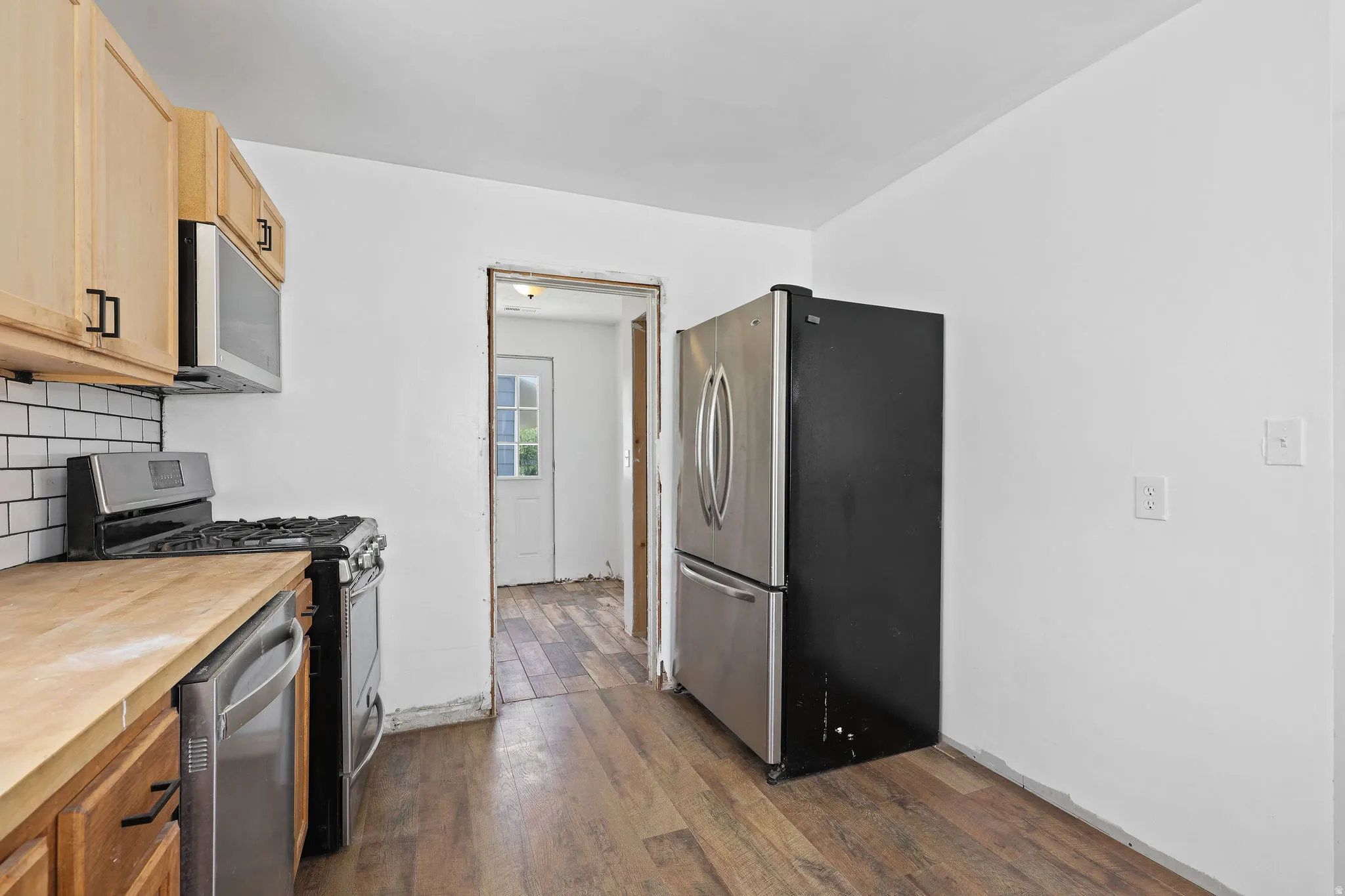 Kitchen featuring wood-finish flooring, light wood cabinetry, butcher block countertops, white subway tile backsplash, and stainless steel appliances