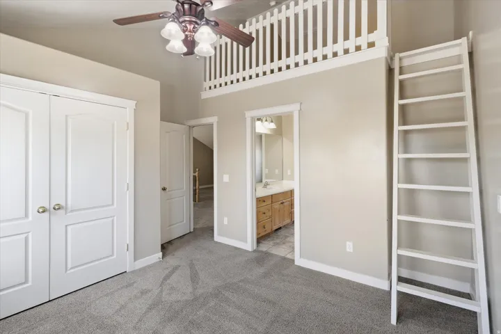 Carpeted room featuring a loft with white railing, a white wooden ladder, and a ceiling fan with light fixture