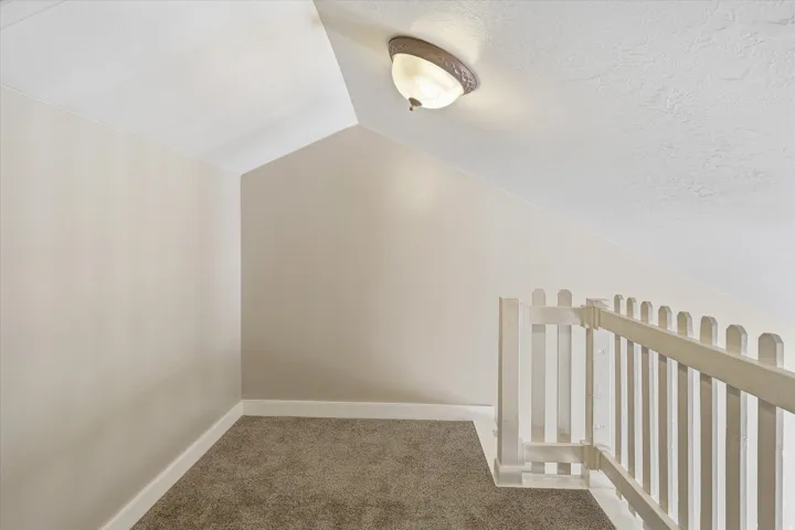 Carpeted loft area featuring sloped ceilings, a semi-flush mount ceiling light, and a white picket-style railing