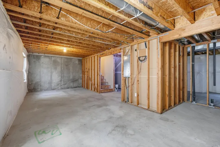 Unfinished basement featuring exposed wood joists, concrete flooring, and framed walls