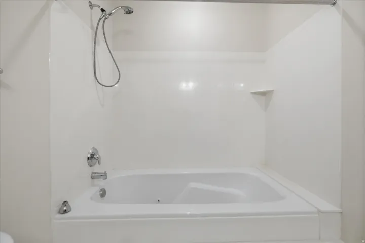 White bathtub with integrated shower, chrome fixtures, and a corner shelf