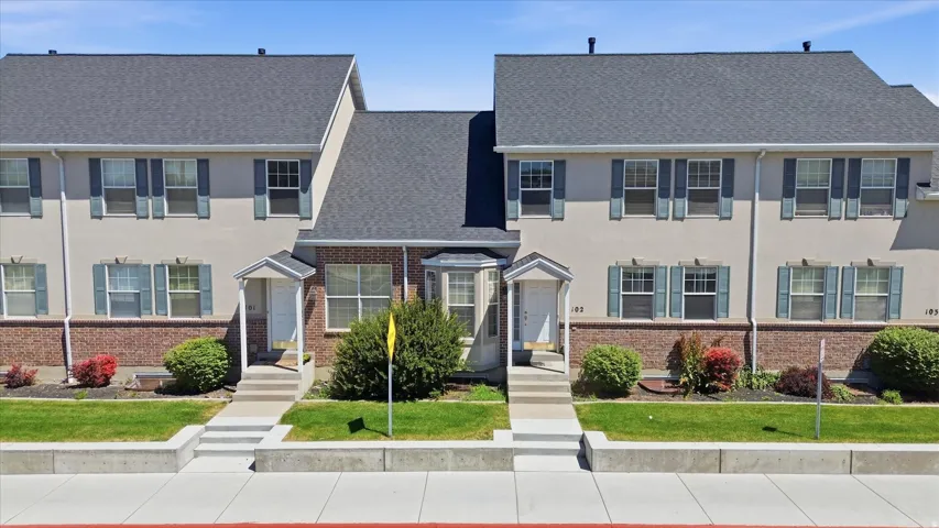 Townhouse exterior featuring a gray shingled roof, light-colored stucco siding, and a brick facade
