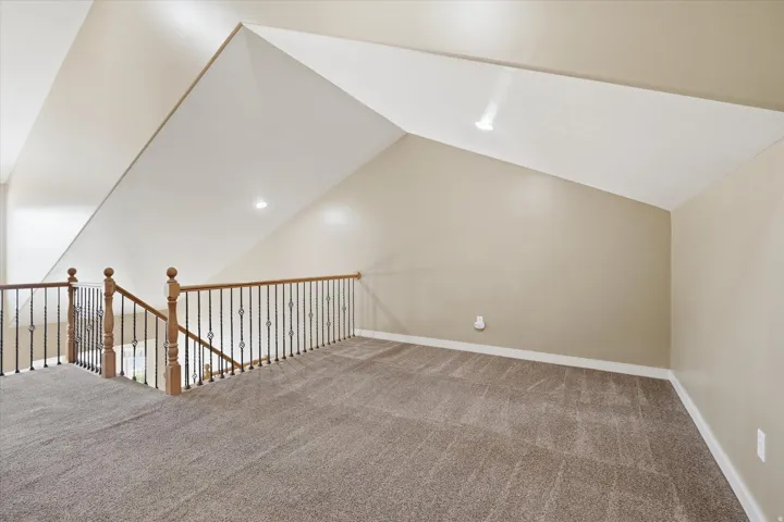 Carpeted loft area featuring a wood handrail with wrought iron balusters, angled ceilings, and recessed lighting