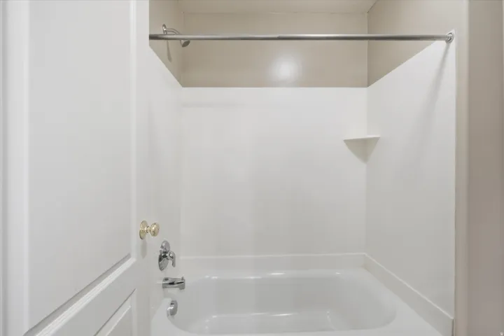 White tub and shower combination featuring a chrome faucet, a corner shelf, and a curved shower rod
