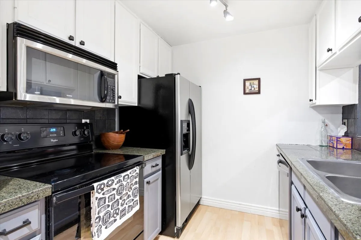 Kitchen featuring white upper cabinetry, light gray lower cabinetry, and a black tile backsplash