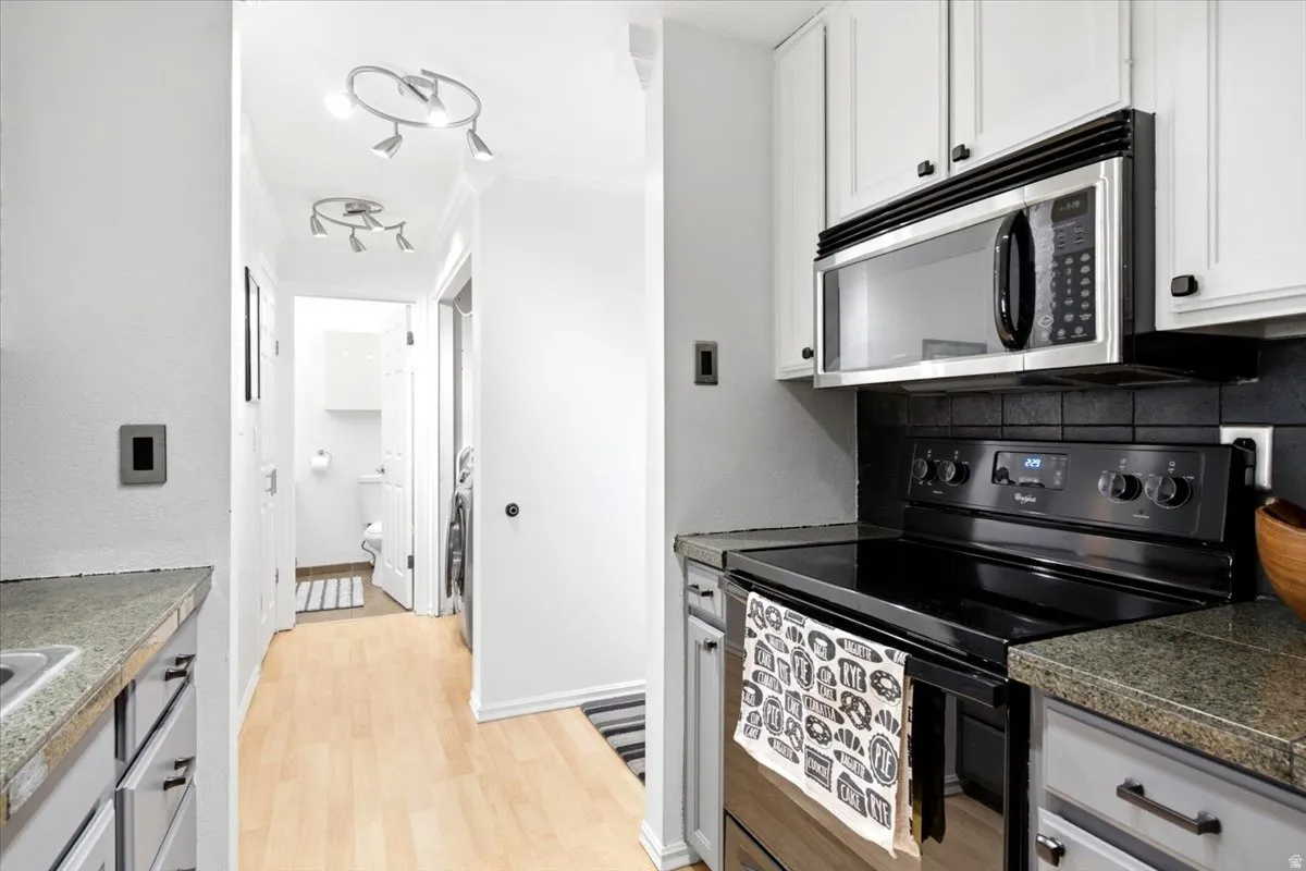 Kitchen with stainless steel over-the-range microwave, black electric range, and light-colored cabinetry with dark hardware