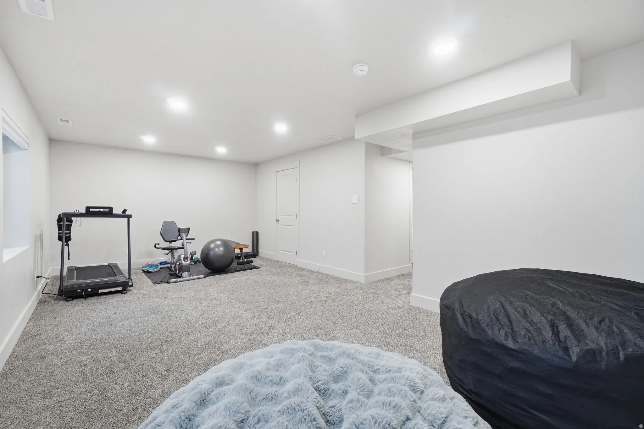 Spacious finished basement room featuring light gray carpet, recessed lighting, white walls, and white baseboards