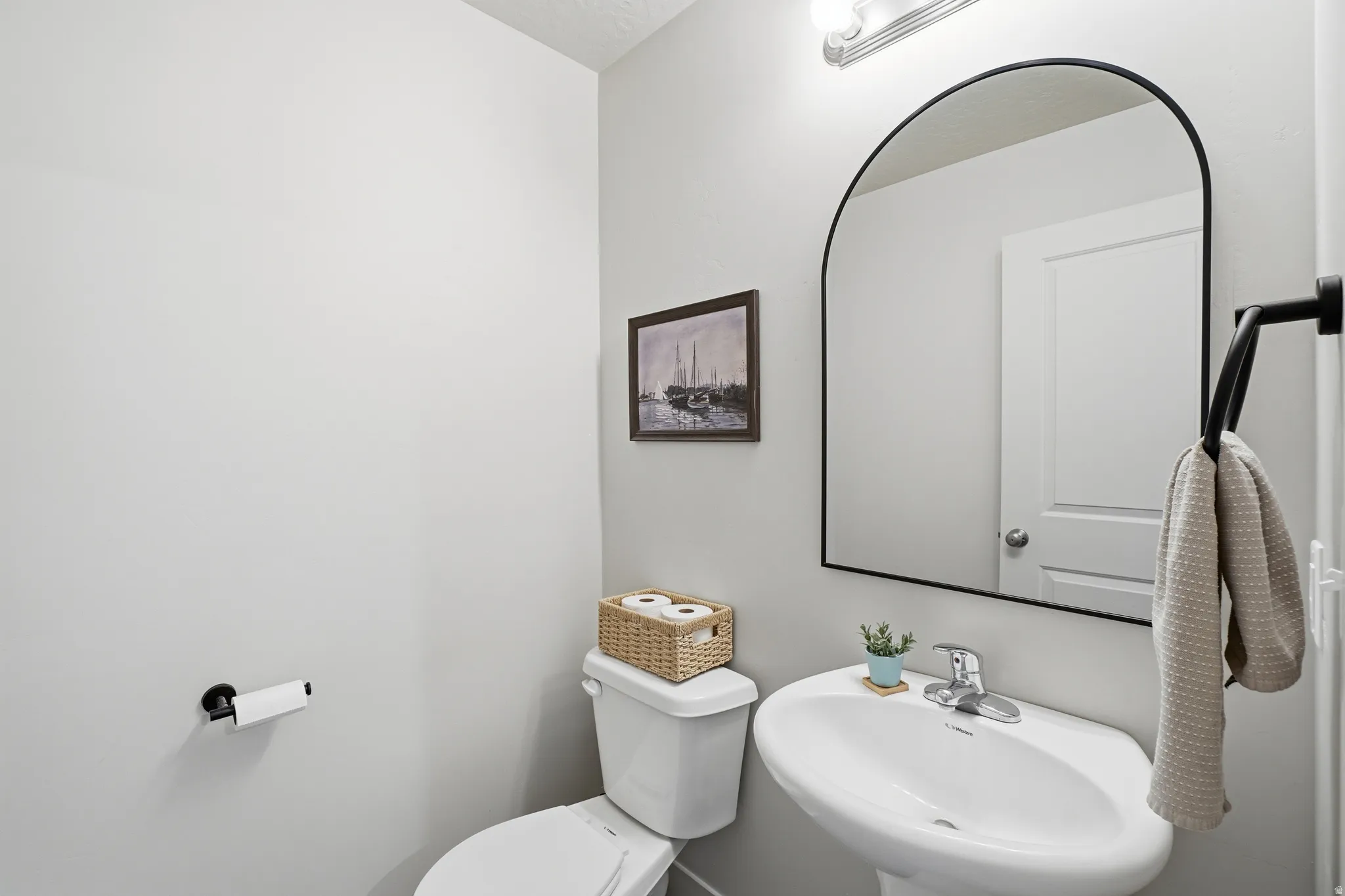 White pedestal sink with a chrome faucet, illuminated by a vanity light fixture