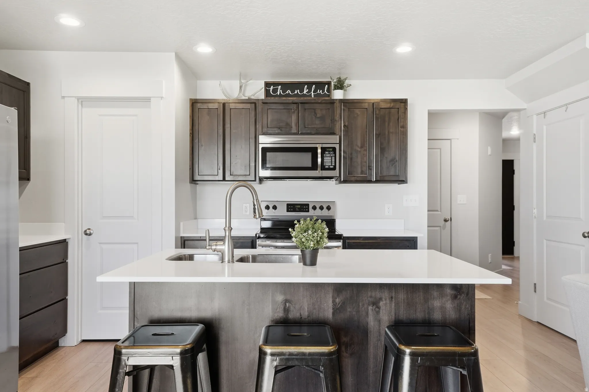 Kitchen featuring a central island with white countertop, dark wood-finish cabinetry, stainless steel appliances, and recessed lighting