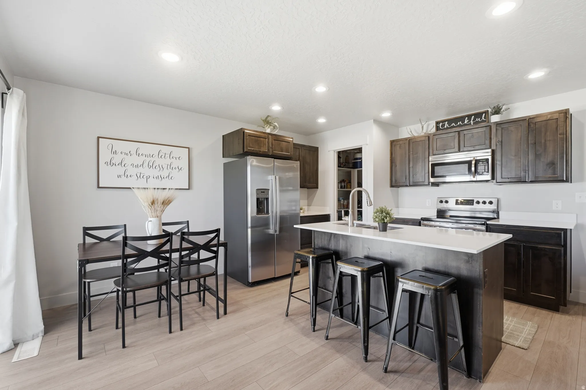 Open-concept kitchen featuring wood-finish flooring, dark wood cabinetry, stainless steel appliances, a center island with seating, and recessed lighting