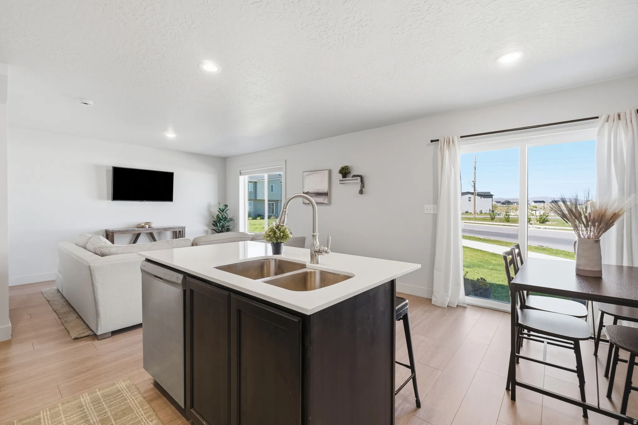 Open-concept living space featuring a central kitchen island with dual stainless steel sinks, white countertops, and dark cabinetry