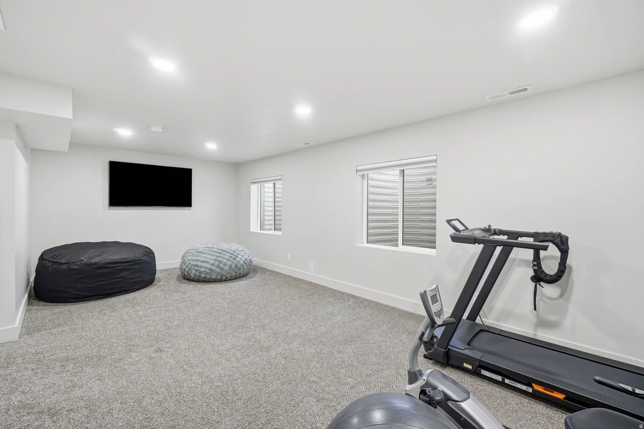 Basement family room featuring light gray carpeting, recessed lighting, and a wall-mounted flat-screen television
