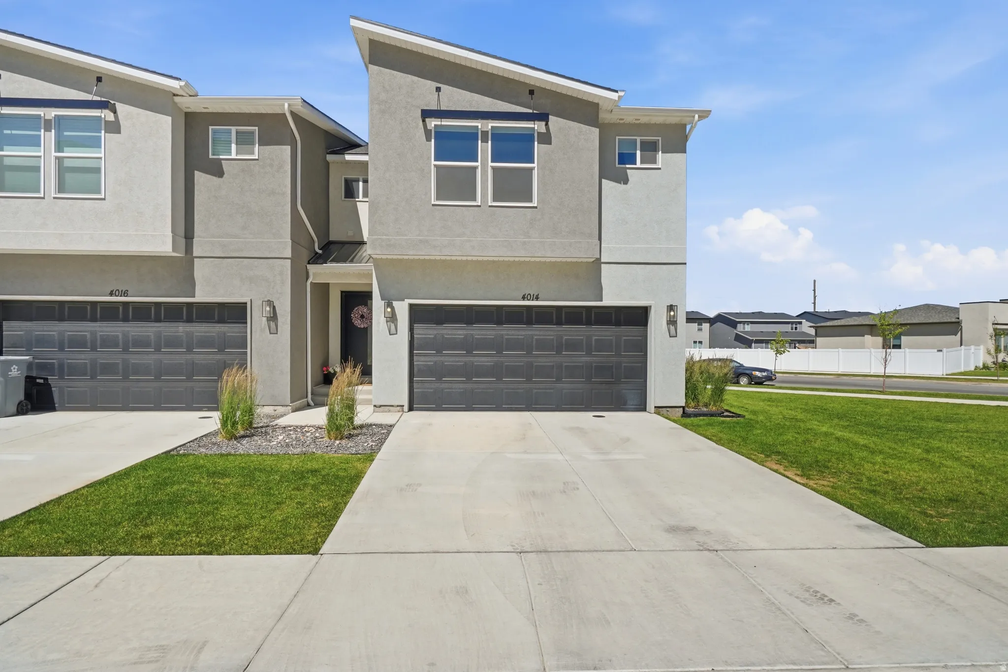 Modern townhome exterior featuring contemporary grey stucco, dual single-car garages, and concrete driveways