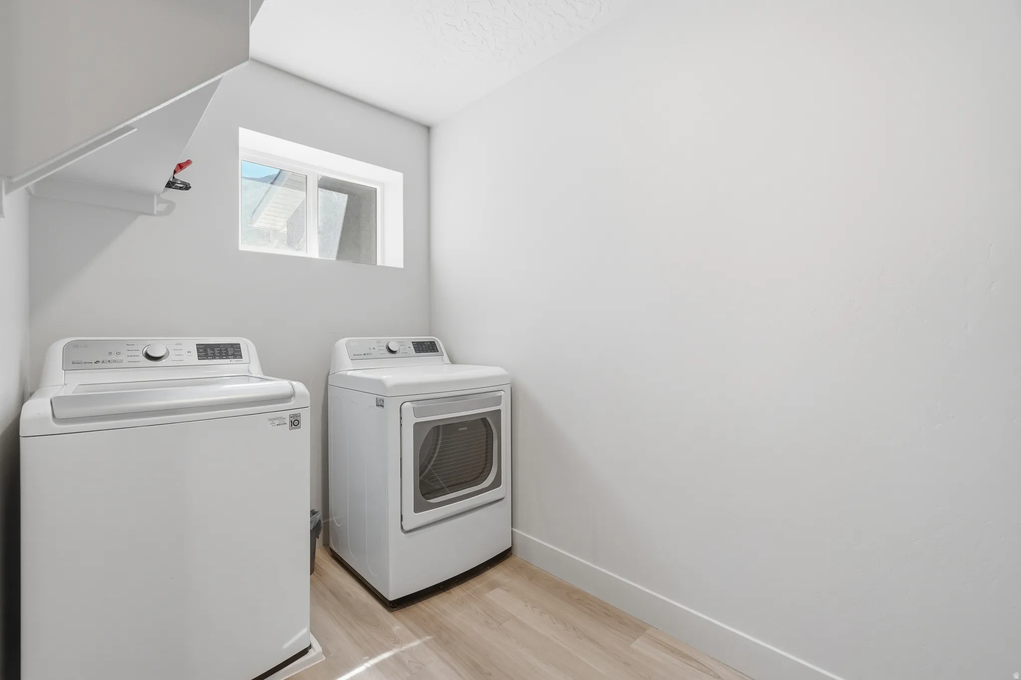 Dedicated utility area featuring wood-finish flooring, a white baseboard, a high window, and a built-in shelf