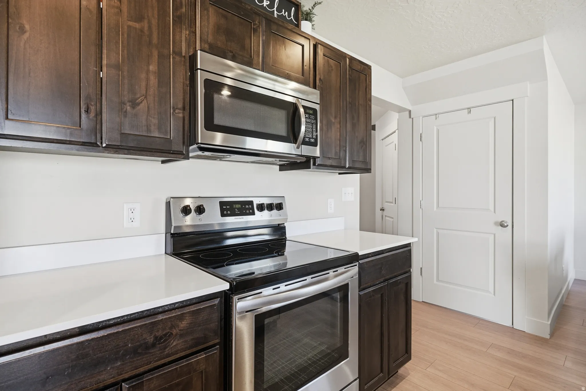 Stainless steel range with a built-in microwave, dark wood cabinetry, and light countertops