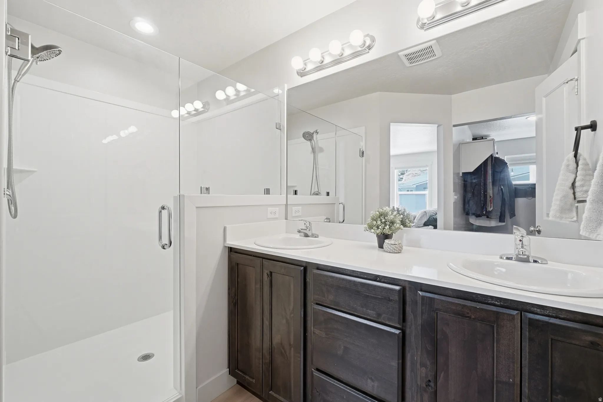 Bathroom featuring a glass-enclosed walk-in shower with a chrome shower head, a double vanity with dark wood-finish cabinetry, white countertops, and dual undermount sinks with chrome faucets