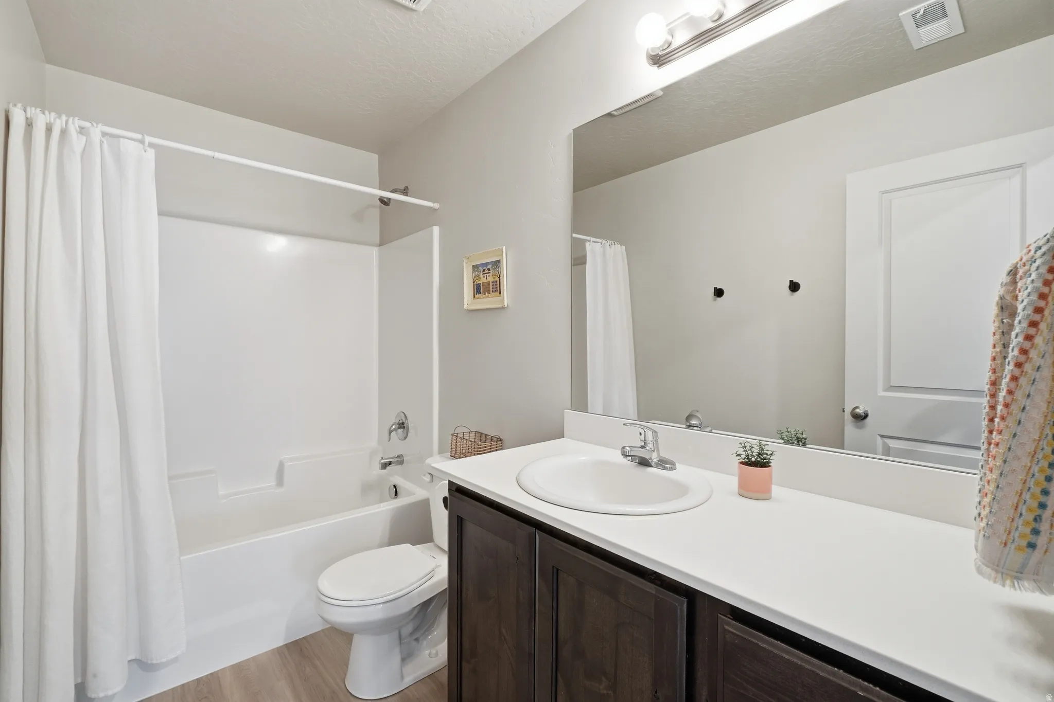 Bathroom featuring a white integrated tub and shower unit, a dark wood-finish vanity with a white countertop, and a large wall-mounted mirror